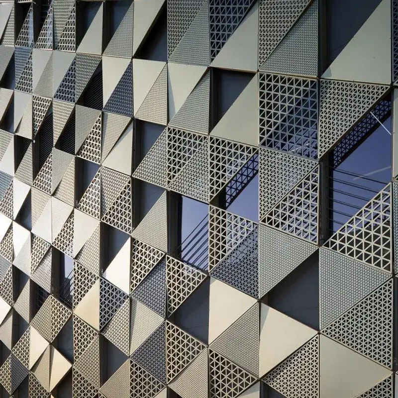 An intricate geometric pattern made from aluminum perforated panels covering a building's exterior. The panels feature a combination of triangles and diamond shapes, creating a dynamic and eye-catching design.