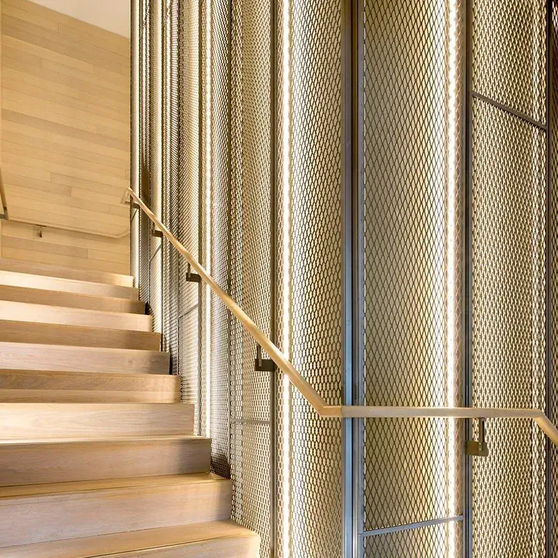 The wall next to the exhibition staircase is decorated with mesh aluminum panels.